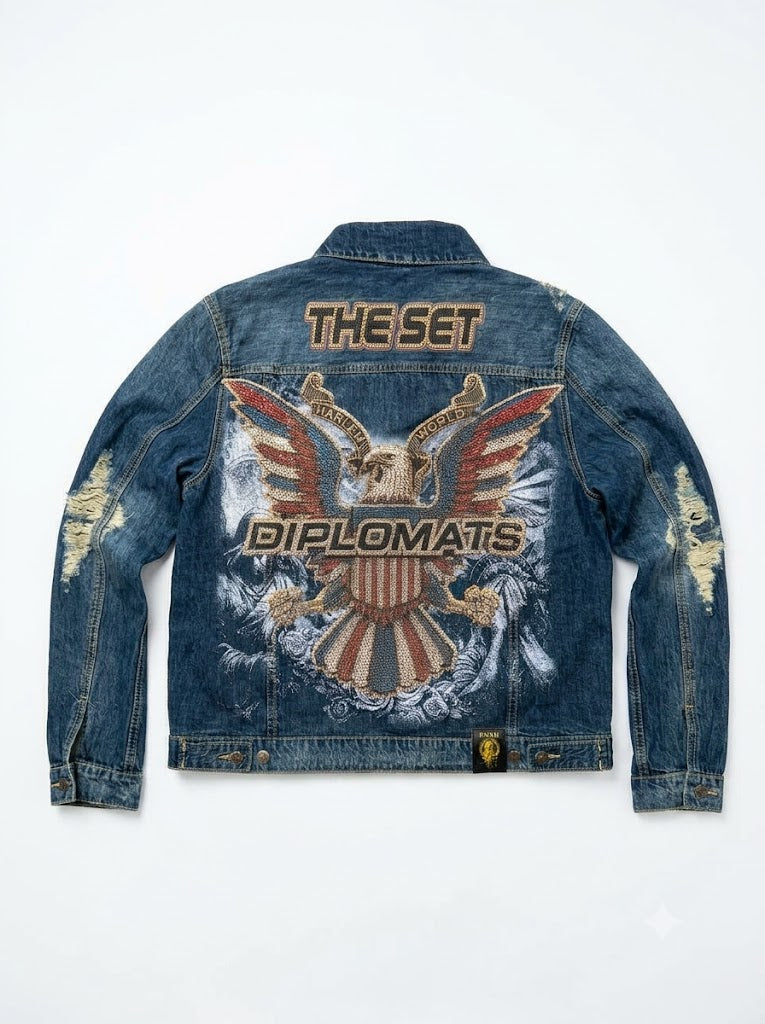A blue denim jacket shown from the back, featuring a large patriotic eagle graphic with the words 'THE SET' and 'DIPLOMATS' in gold lettering, along with distressed details on the sleeves.