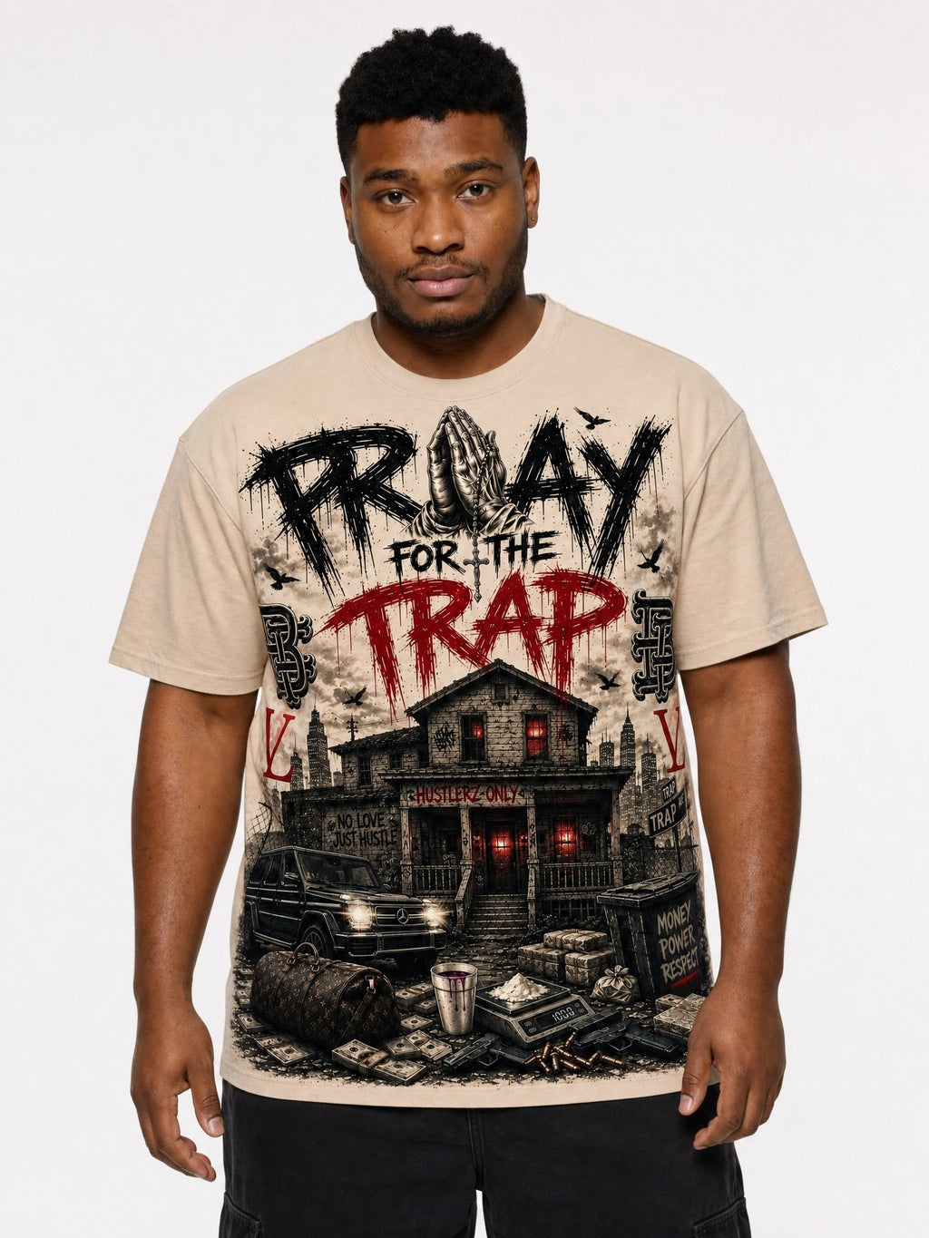 A man wearing a beige graphic t-shirt with a detailed black and red print that reads 'PROAY FOR THE TRAP' above an illustration of a haunted house and a car, set against a plain light gray background.